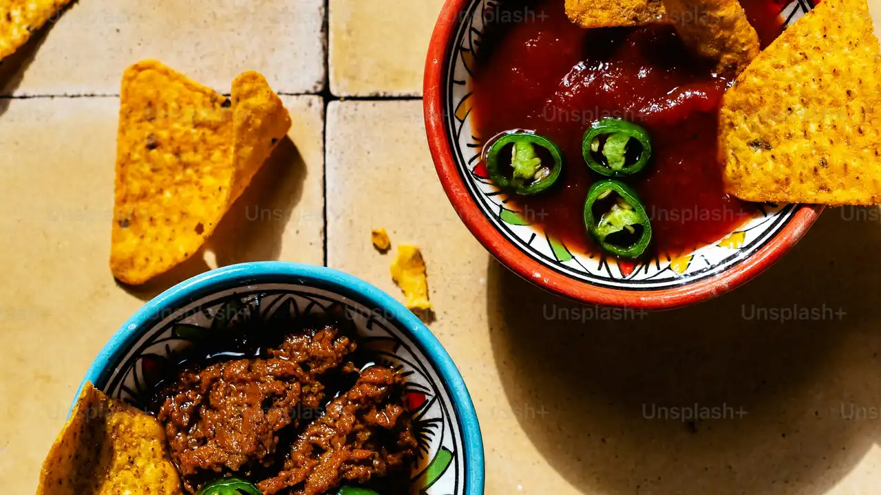 blue bowl of black bean beef tortilla soup on a board with cilantro and shredded cheese in background
